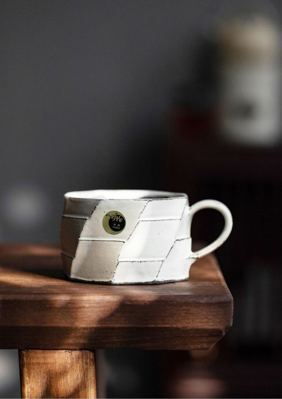 Rustic hand-made carved white stoneware mug from Japan on a wooden table.