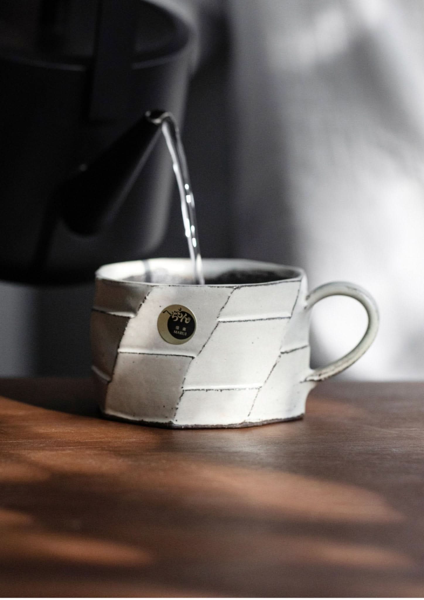 Rustic hand-made carved white stoneware mug from Japan being filled with water on a wooden surface.