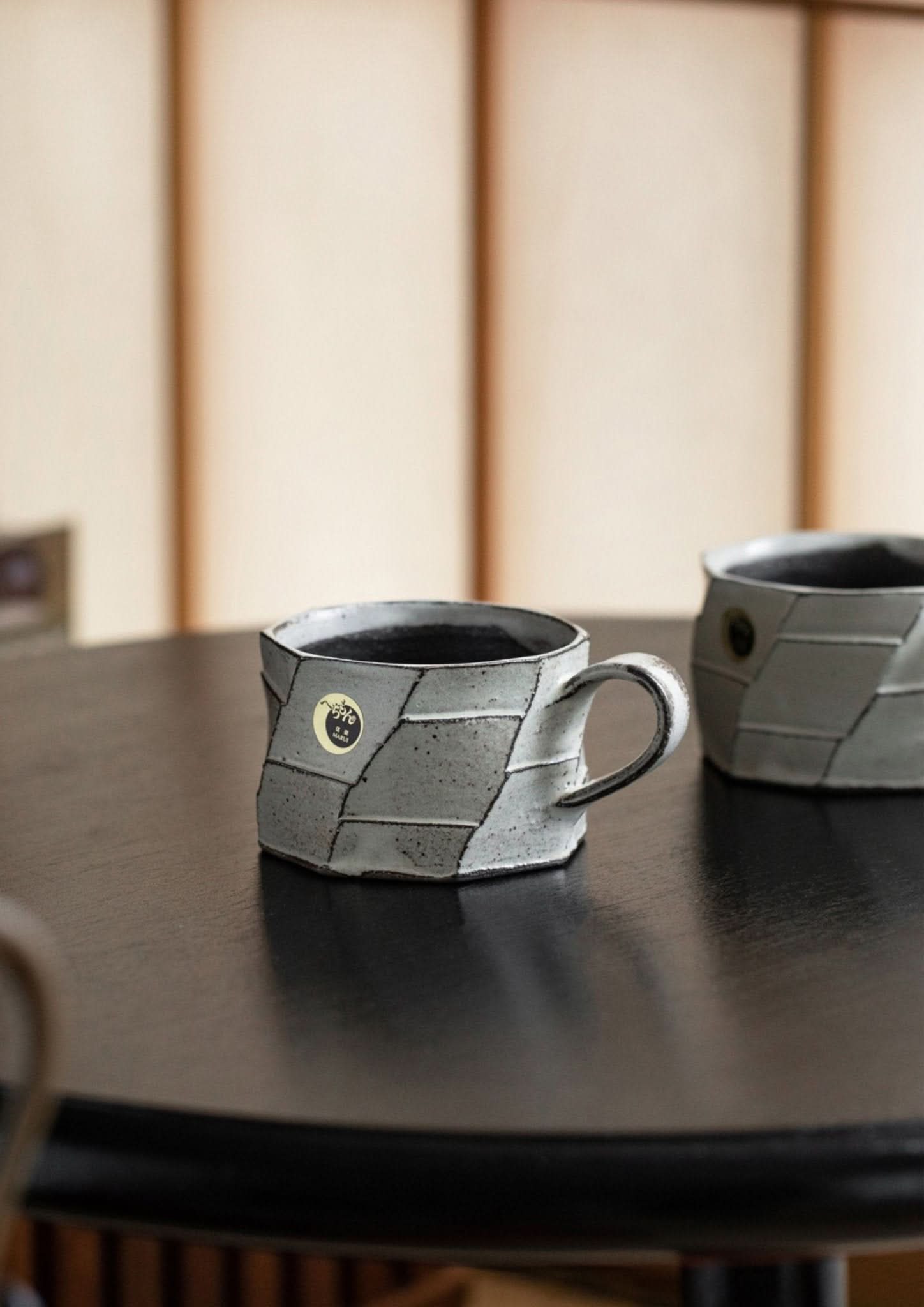 Rustic Japanese carved stoneware mug with unique geometric pattern on dark wood surface.