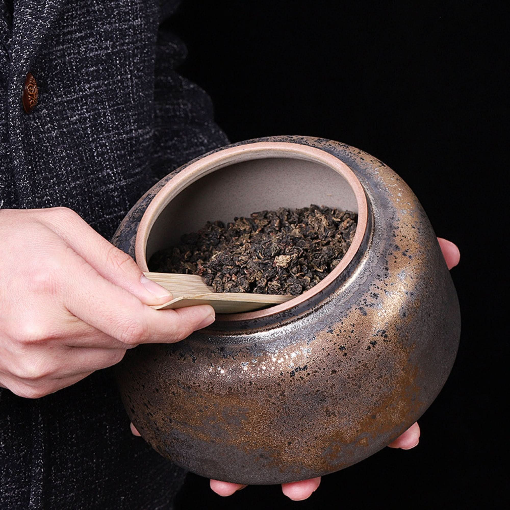 Rustic Traditional Chinese Ceramic Tea Can with tea leaves and bamboo scoop.
