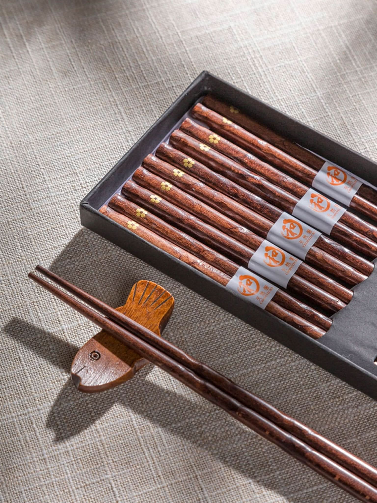 Set of 5 dark wood chopsticks with gold cherry leaf detail, on textured beige background