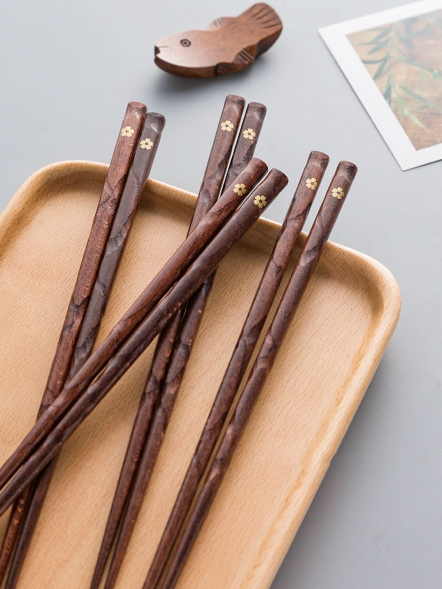 Set of 5 dark wood chopsticks with gold cherry leaf detail on wooden tray.