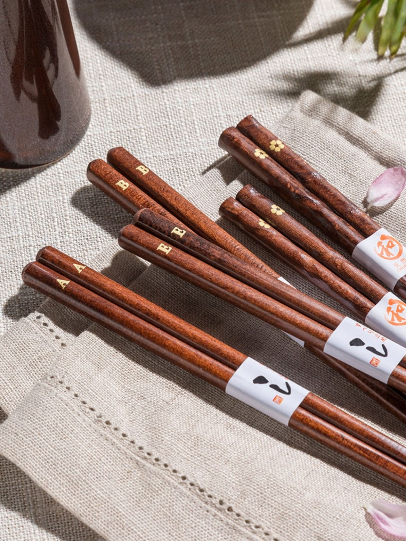 Set of 5 dark wood chopsticks with gold cherry leaf accents on linen.