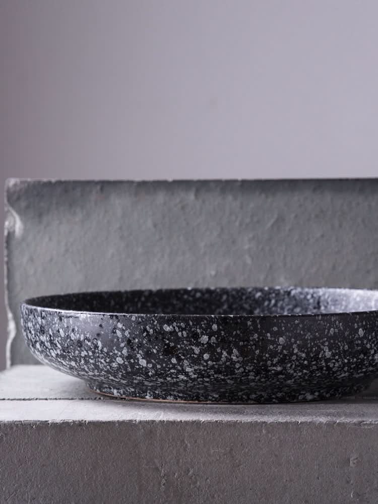 Speckled black ceramic shallow plate and salad bowl with gradient background.