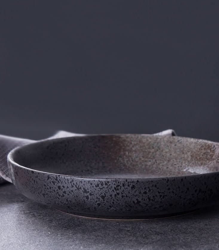 Shallow Plates With Gradients: dark ceramic salad bowl with speckled texture and subtle color gradient.