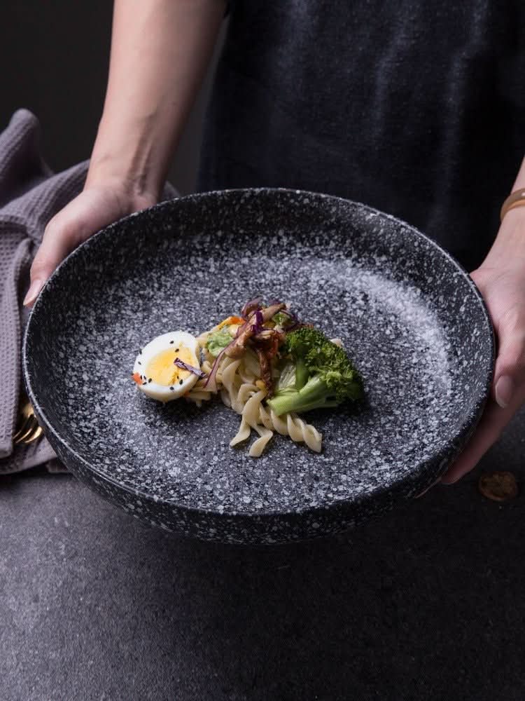 Shallow plates with gradients in speckled black ceramic hold a colorful salad.