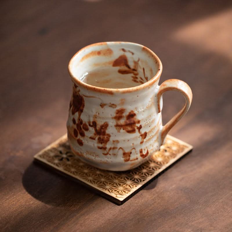 Shino-Yaki ceramic mug, rustic brown floral pattern, on geometric coaster.