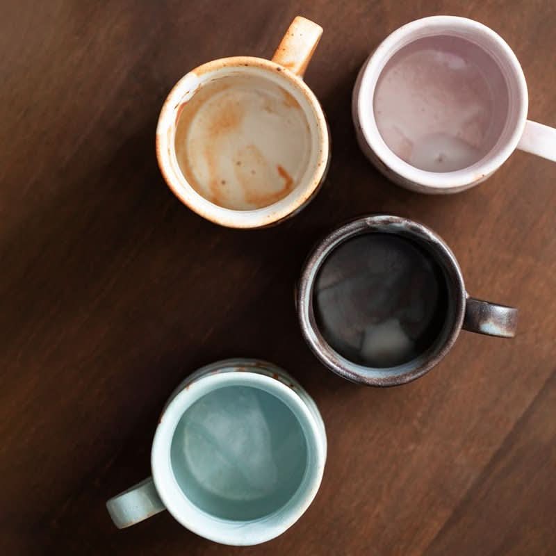 Rustic Shino-Yaki ceramic mugs in earth tones & soft pastels on a wooden surface.