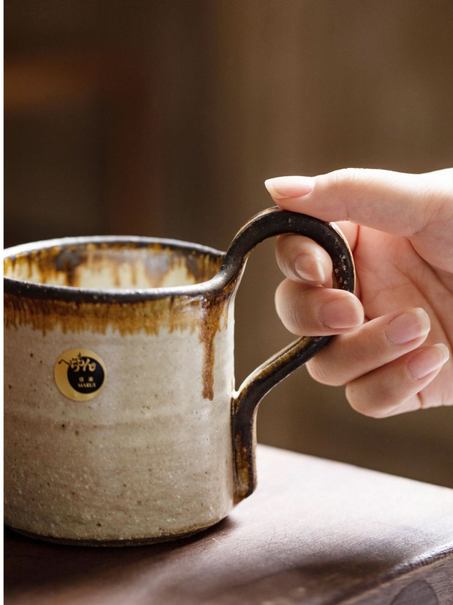 Hand holds rustic Shiraku-yaki stoneware mug, 10.1oz. Earthy glaze, Japanese pottery.