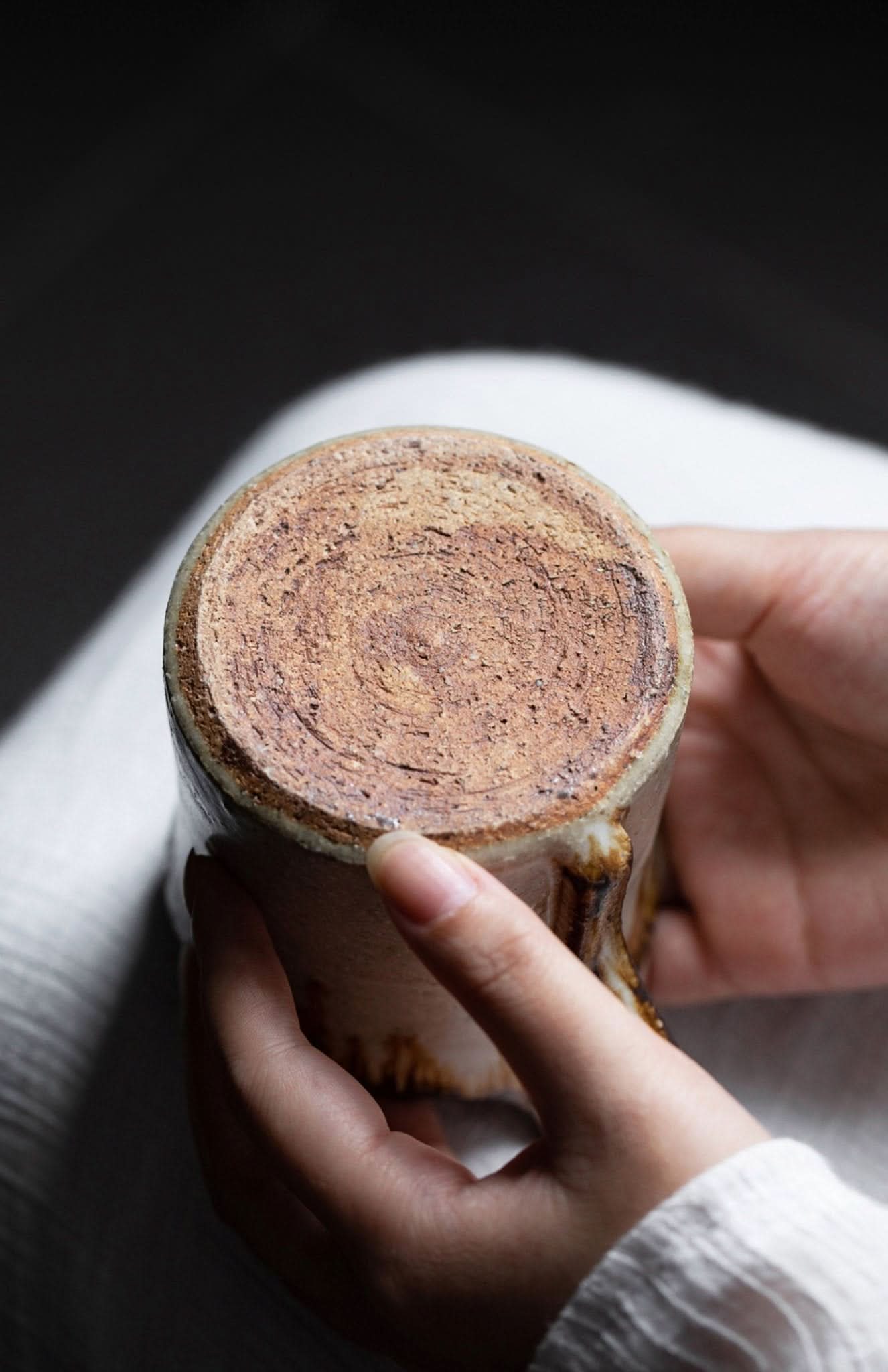 Hands hold Shiraku-yaki stoneware mug, showing rustic, glazed pottery base.