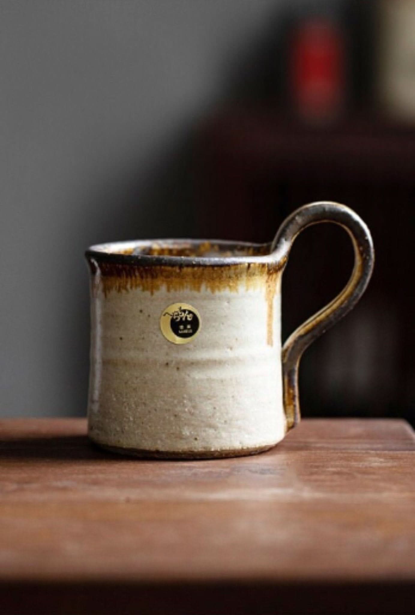Rustic Shiraku-yaki stoneware mug from Japan, cream & brown glaze, handmade pottery on wood.