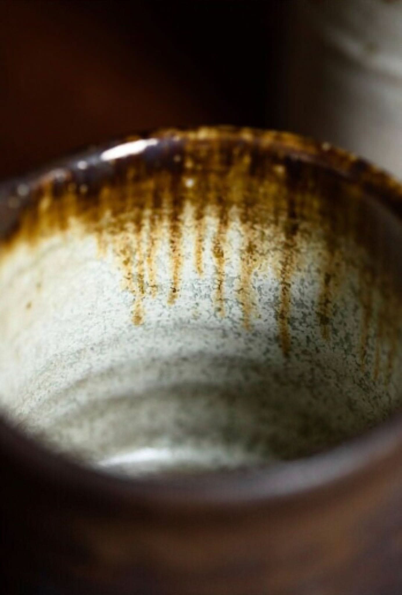 Close-up of Shiraku-yaki stoneware mug interior, rustic glaze with brown drips on white speckled ceramic.