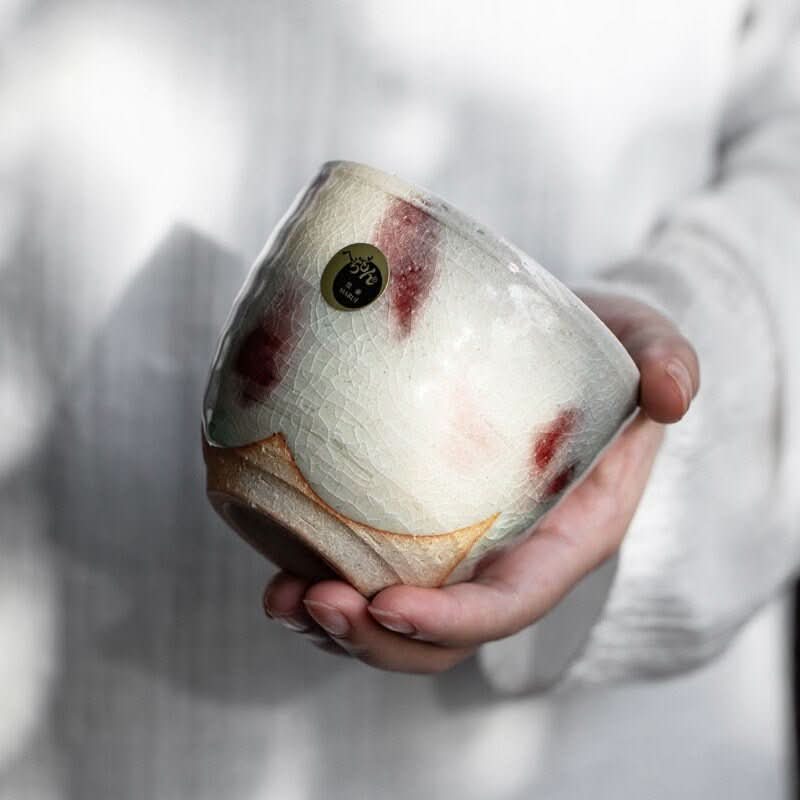 Hand holding a white and red Shiraku-Yaki tea cup with ice cracked glaze, Japanese ceramic.