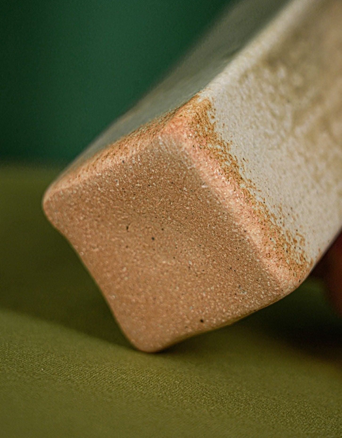 Shigaraki ceramic flower vase, beige with rust accents, on green textured surface.