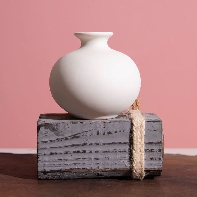 Small ceramic white bud vase on distressed wood block with rope accent. Scandinavian Nordic home decor.