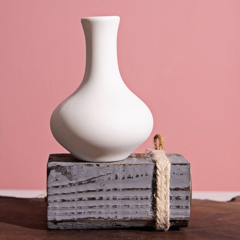 Small ceramic white bud vase on distressed wood block with rope detail.