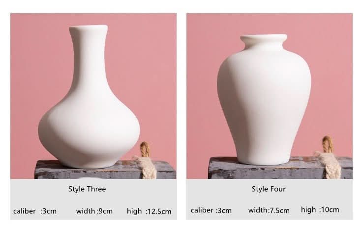 Two white ceramic bud vases, Scandinavian style, on decorative wooden stands against a pink backdrop.