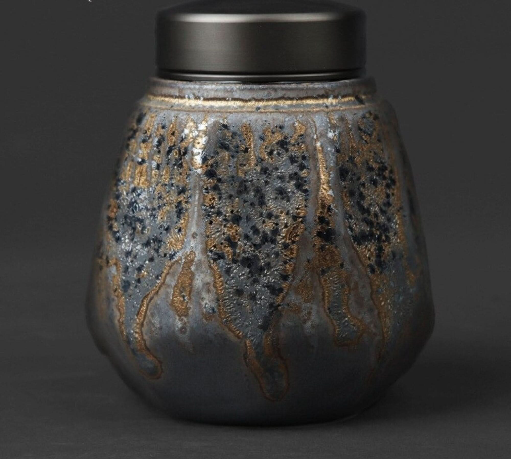 Small stoneware sealed tea can with a textured grey and gold finish on a dark background.