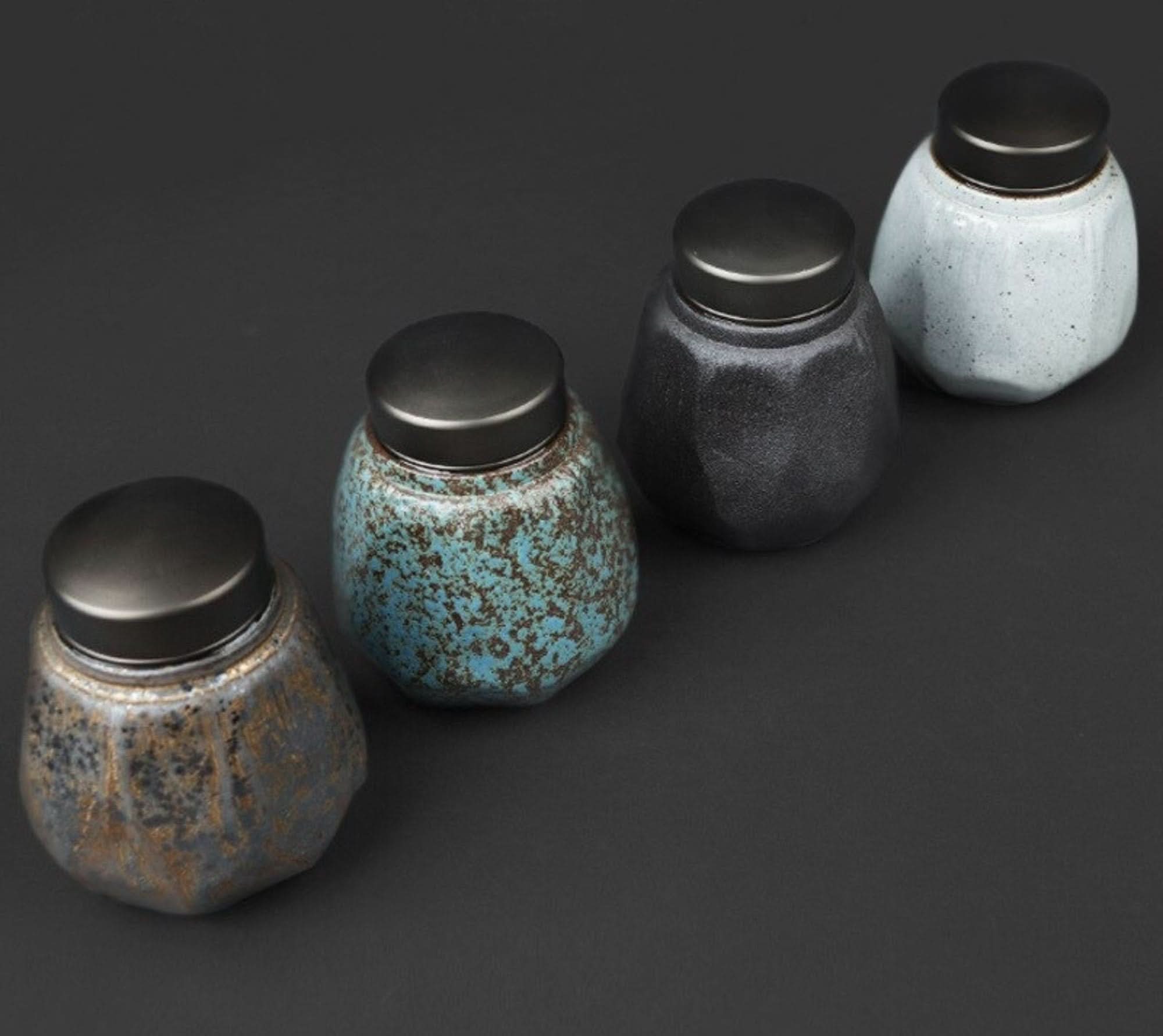 Four speckled small stoneware sealed tea cans in rustic brown, blue, black, and white colors.