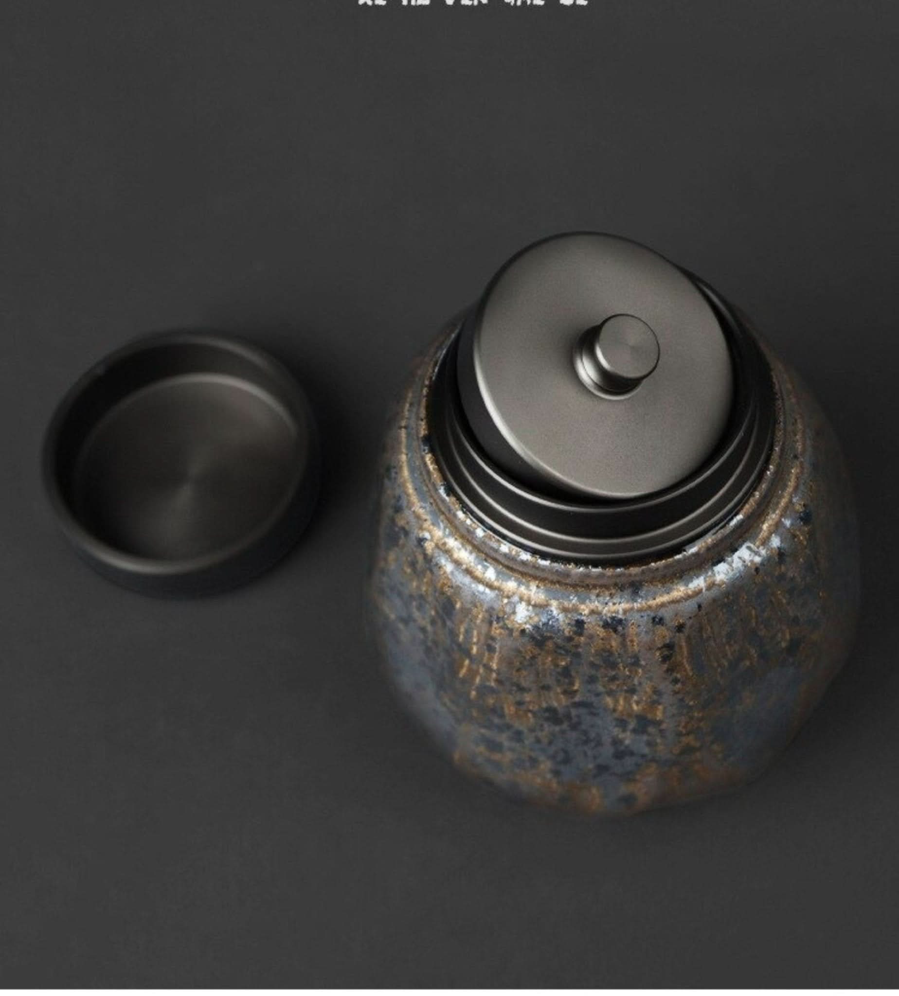Small stoneware sealed tea can with textured blue and gold finish on dark background.