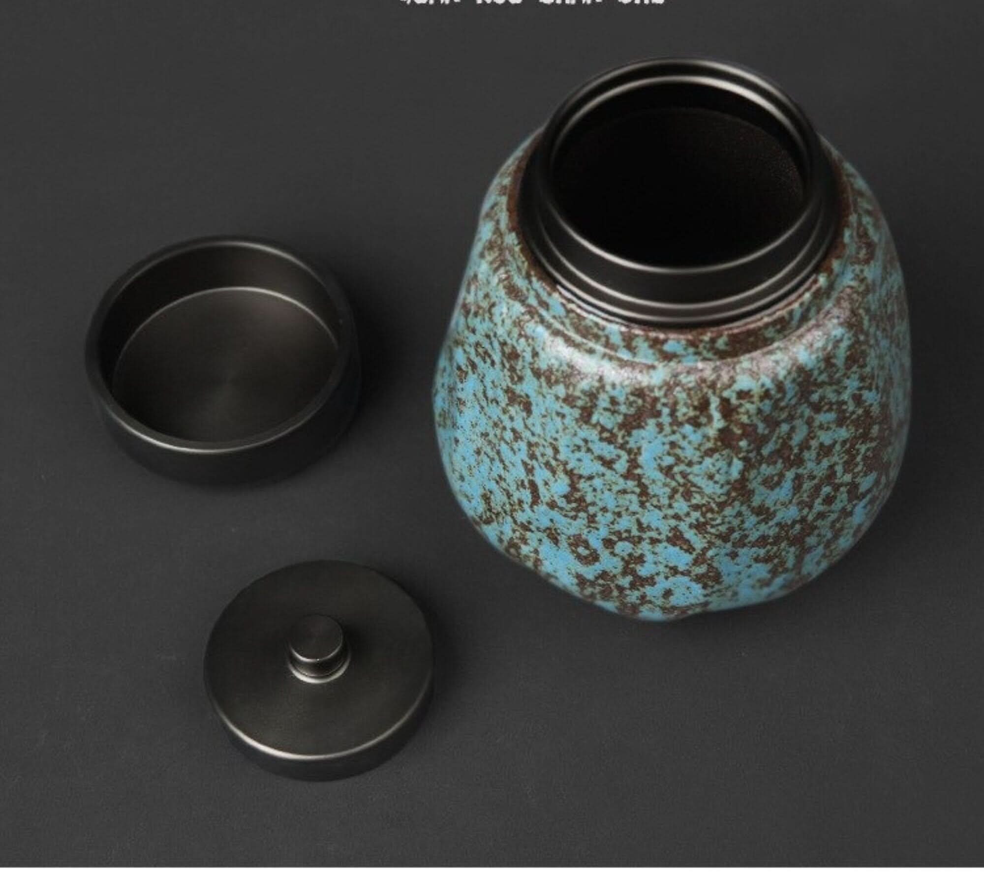 Small stoneware sealed tea can with blue and brown speckle glaze and dark metal lid.