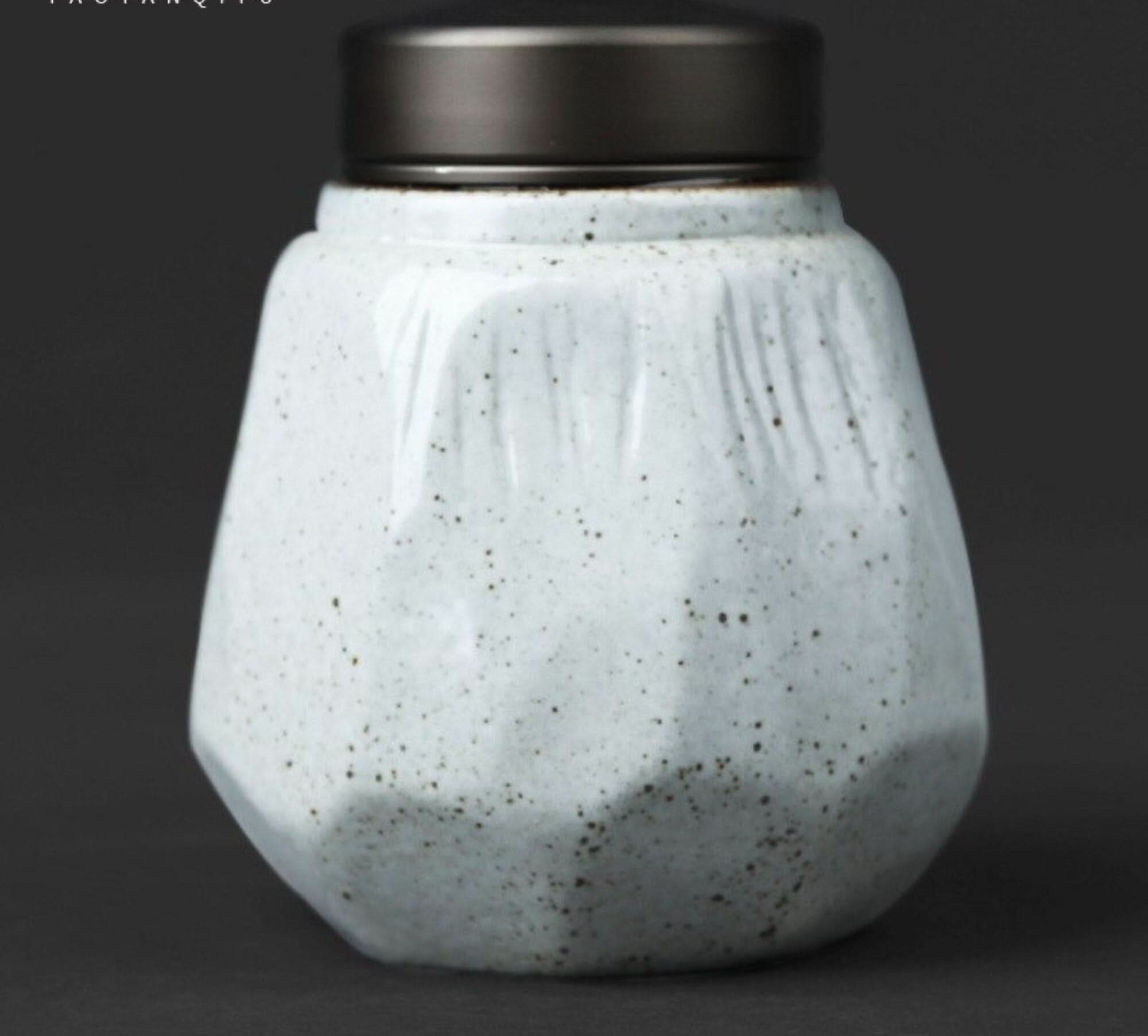 Small speckled stoneware sealed tea can with a dark metal lid on a dark background.