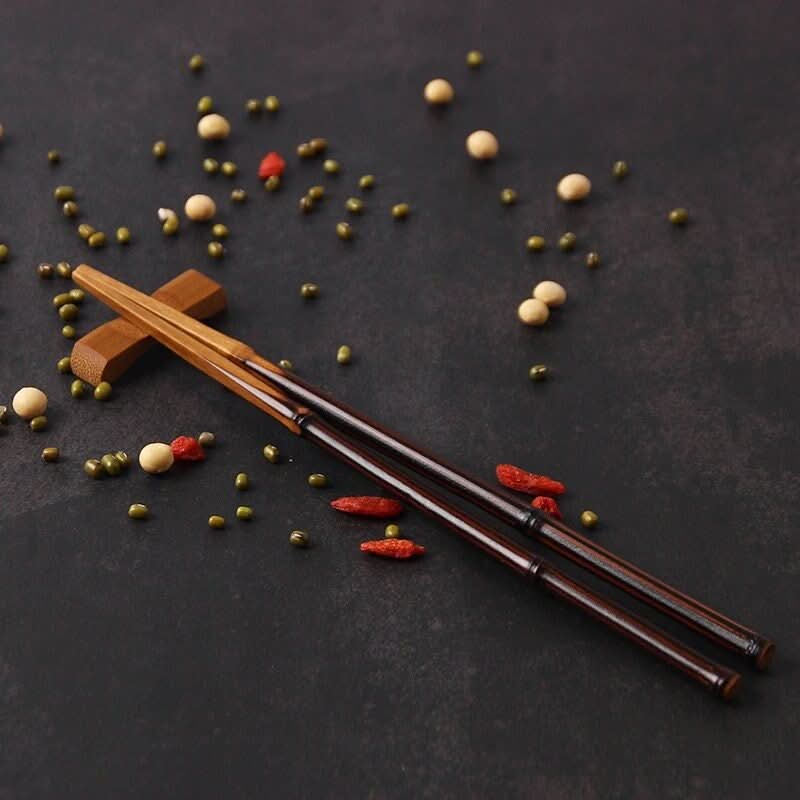 Solid bamboo chopsticks with glossy finish on dark surface with scattered beans and red peppercorns.