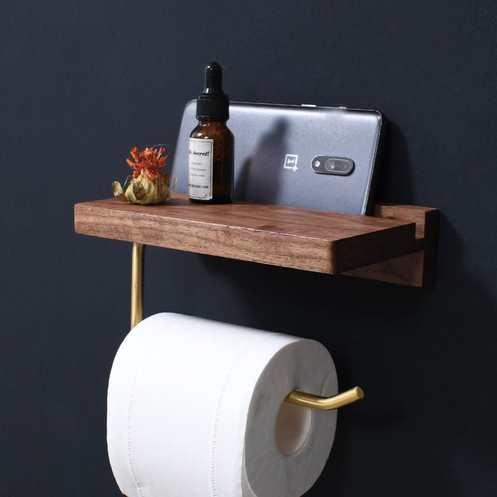 Solid wood and gold toilet paper holder with shelf, holding phone, bottle and decor.