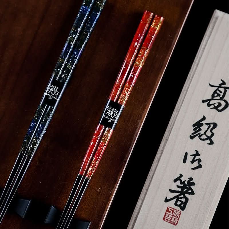 Red and blue handmade lacquered Japanese chopstick set with gold glitter accents, on a wooden surface.
