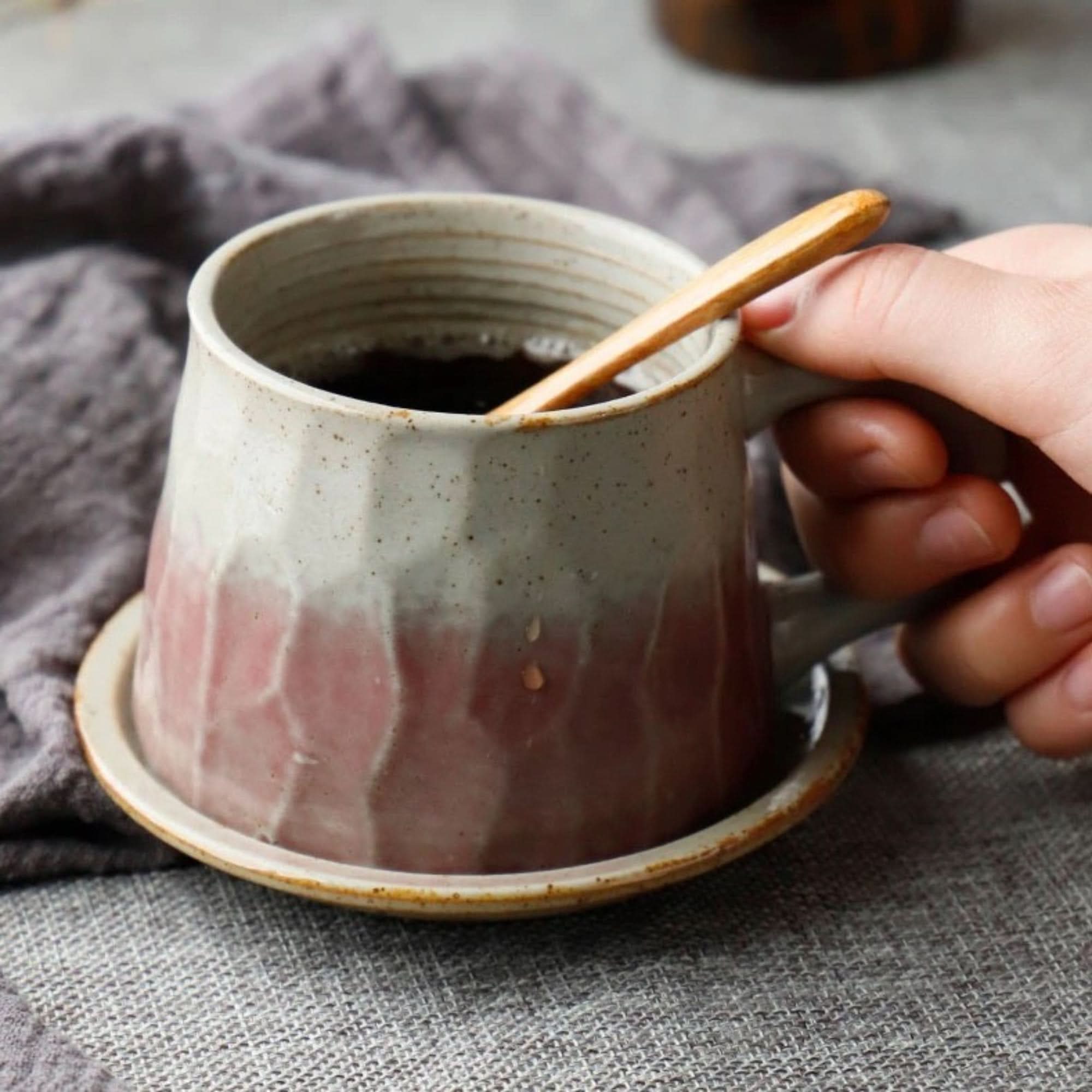 Stoneware Mug 10.14oz +Free Saucer: hand holding speckled mug with pink & white glaze, on saucer, with wooden spoon.