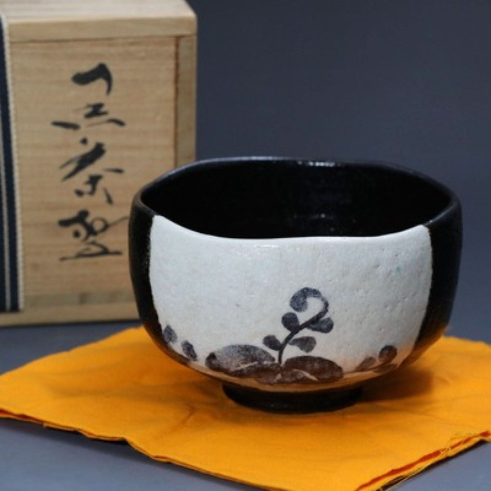 Stoneware Black And White Matcha Bowl With Flowers, hand-painted in Japan, on orange cloth.