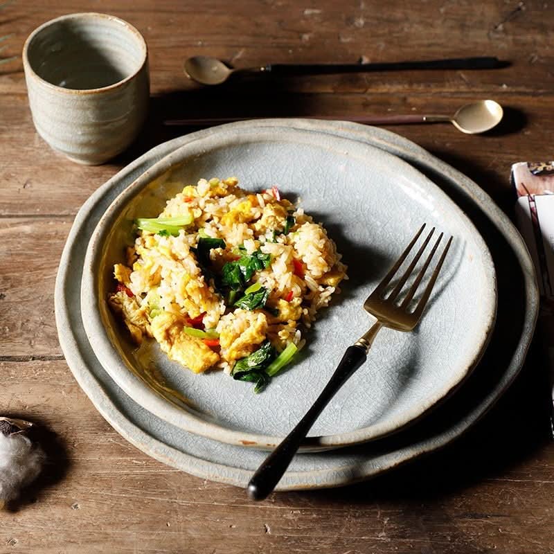Stoneware handmade irregular ice cracked ceramic tableware with fried rice and fork on rustic wood.