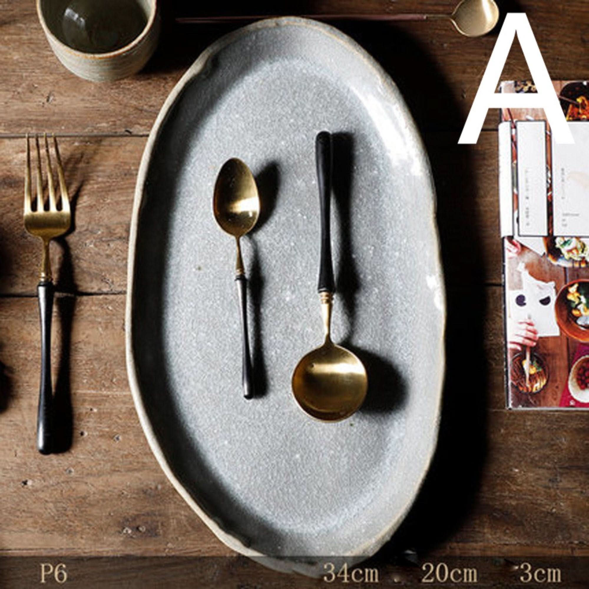 Stoneware Handmade Irregular Ice Cracked Ceramic Tableware, grey oval plate with gold & black spoons, fork on wood.