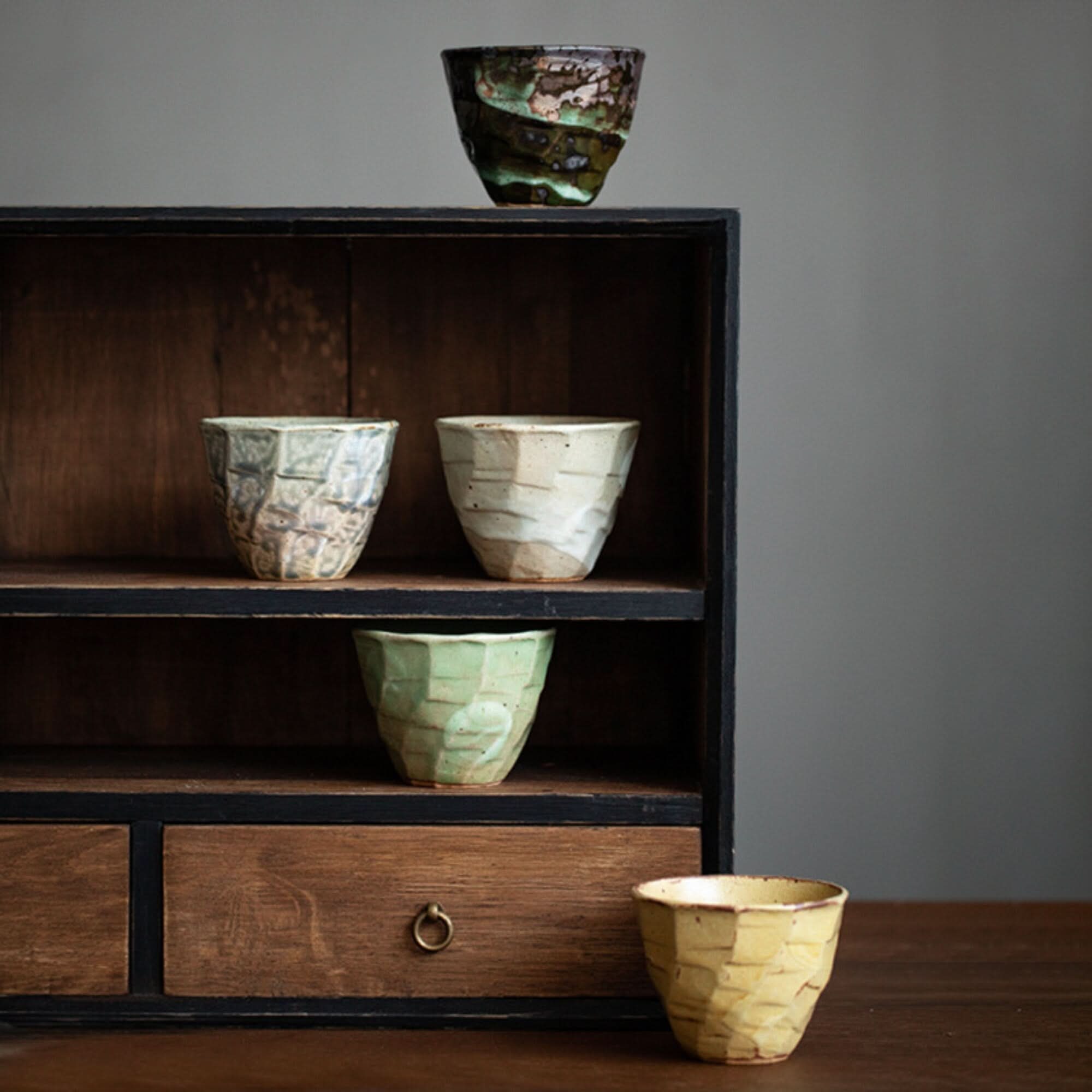Japanese Cups Set 9.4oz: textured ceramic cups in earthy tones displayed on wooden shelves.