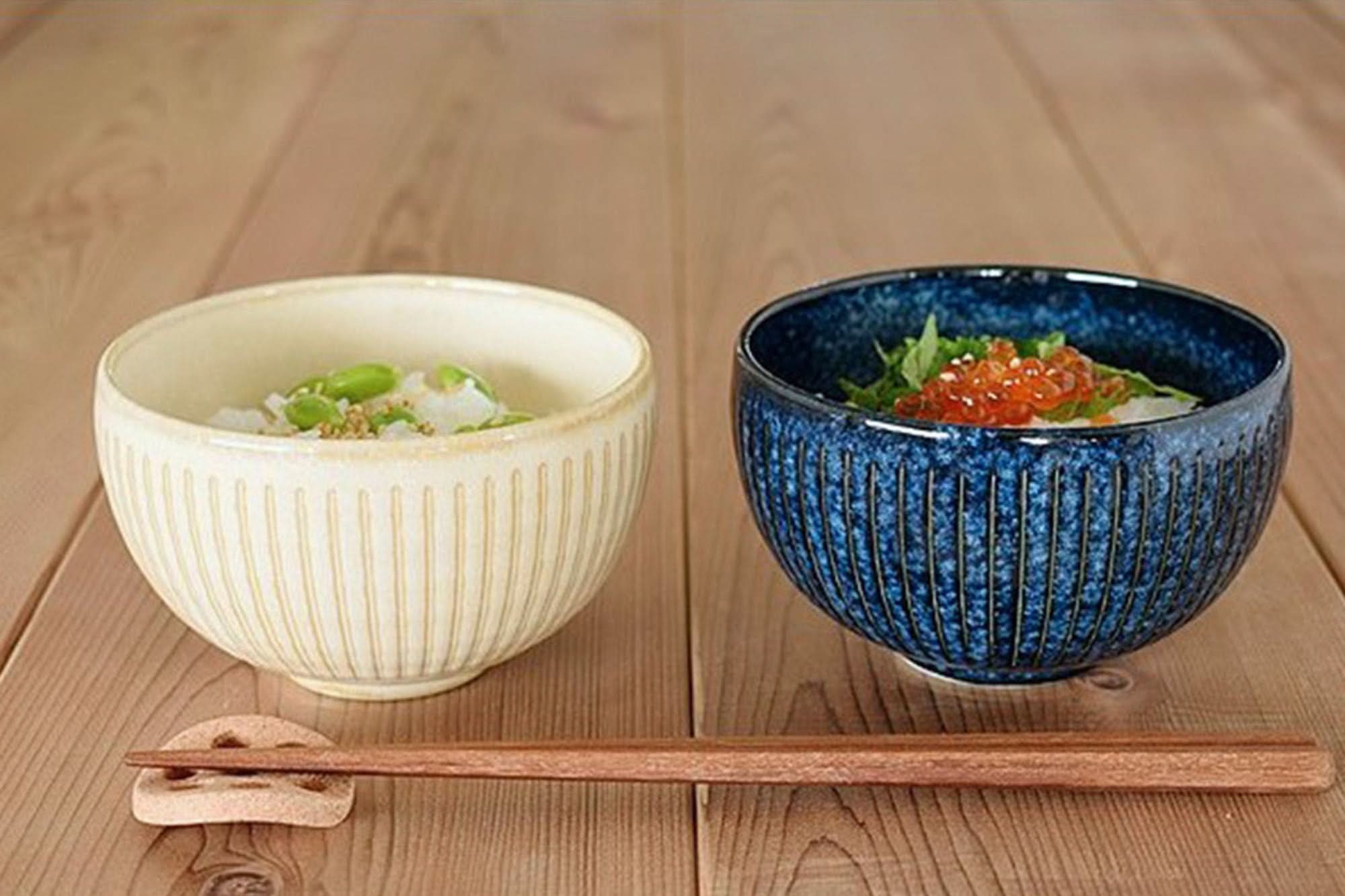 Two Japan imported stoneware soup bowls: one cream, one blue, with chopsticks on wooden surface.