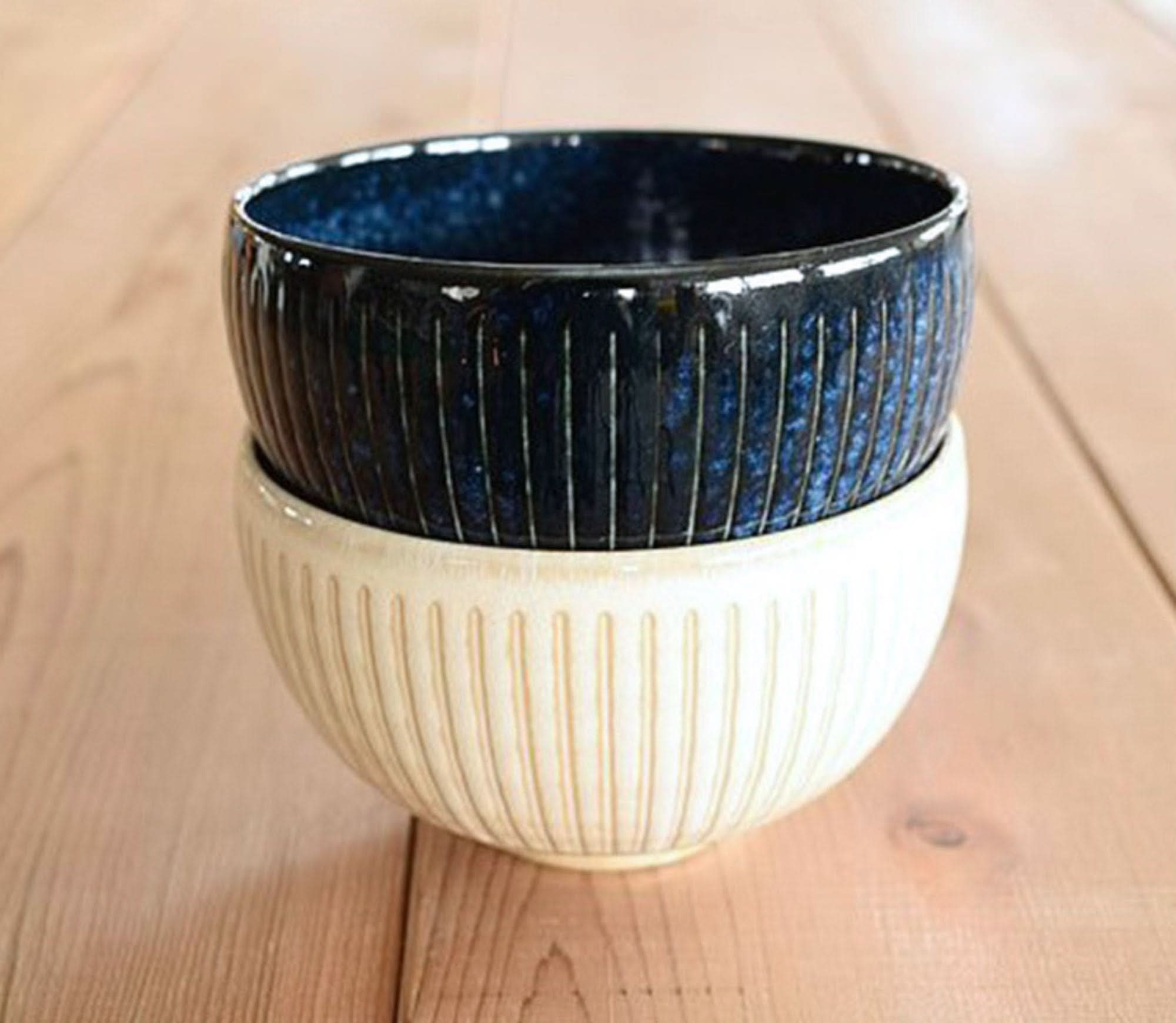 Two Japanese stoneware soup bowls stacked, one dark blue with vertical lines, one cream colored.