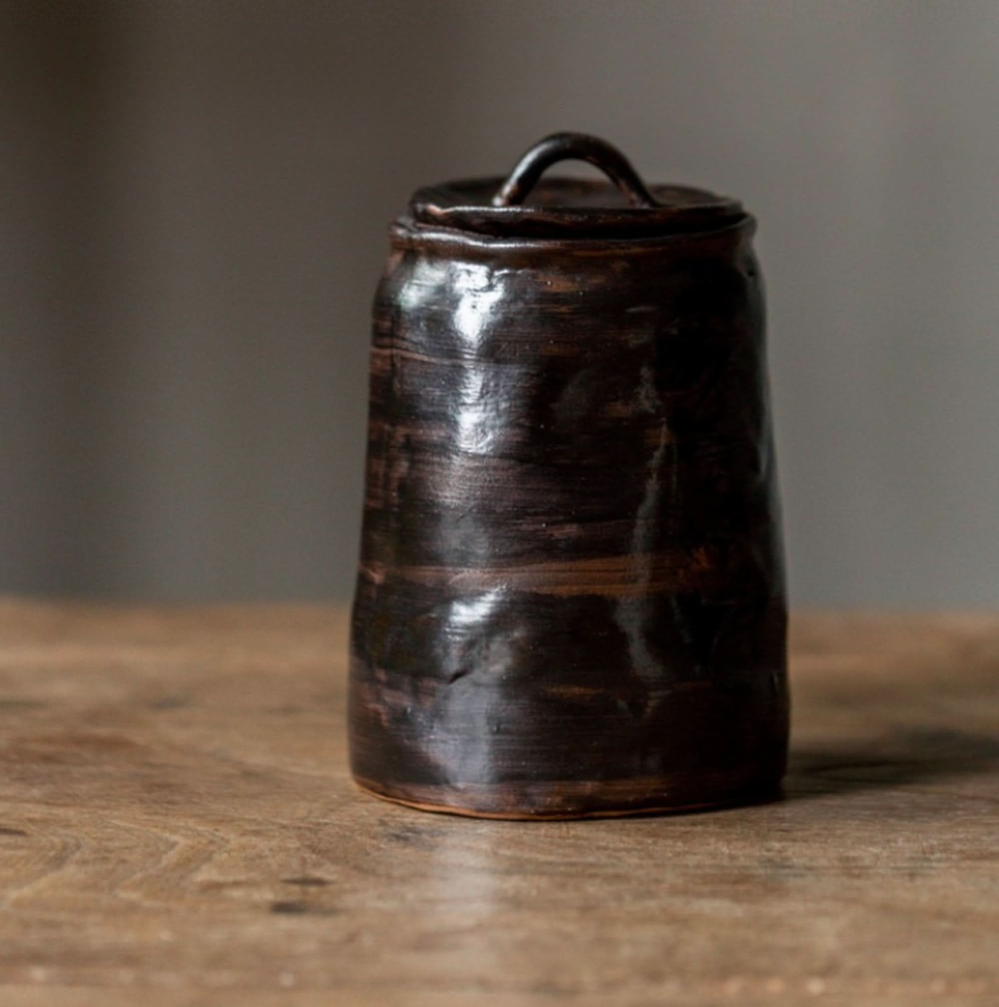Dark stoneware tea canister with textured glaze and lid, on a wooden surface.