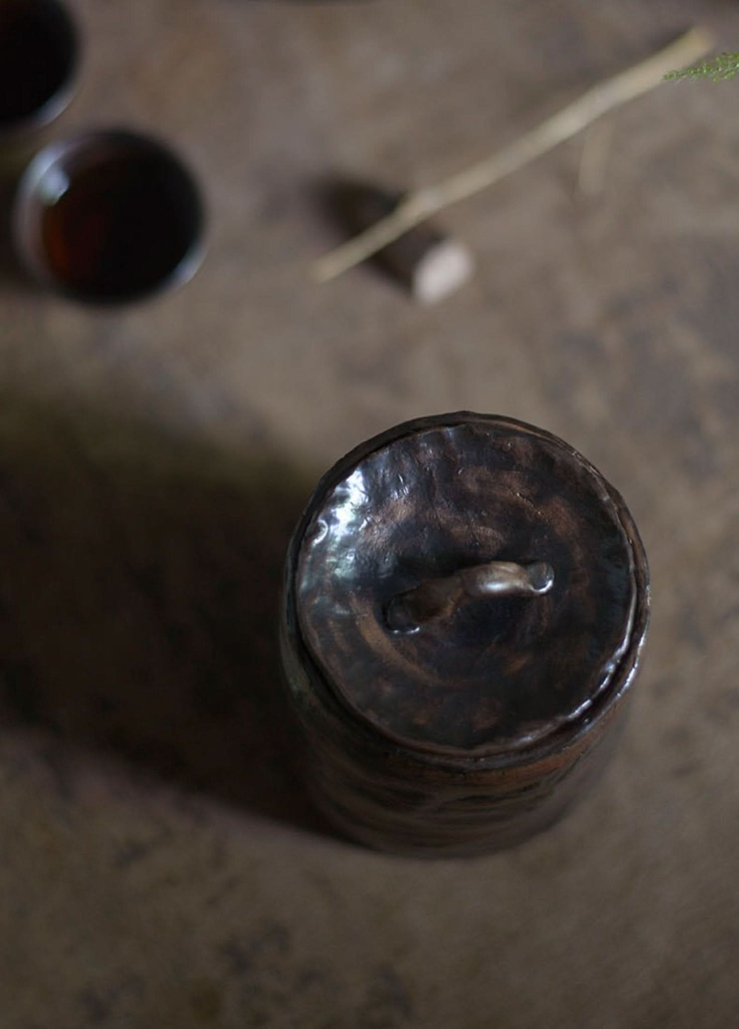 Dark stoneware tea canister, Gongfu tea serving, on textured surface.
