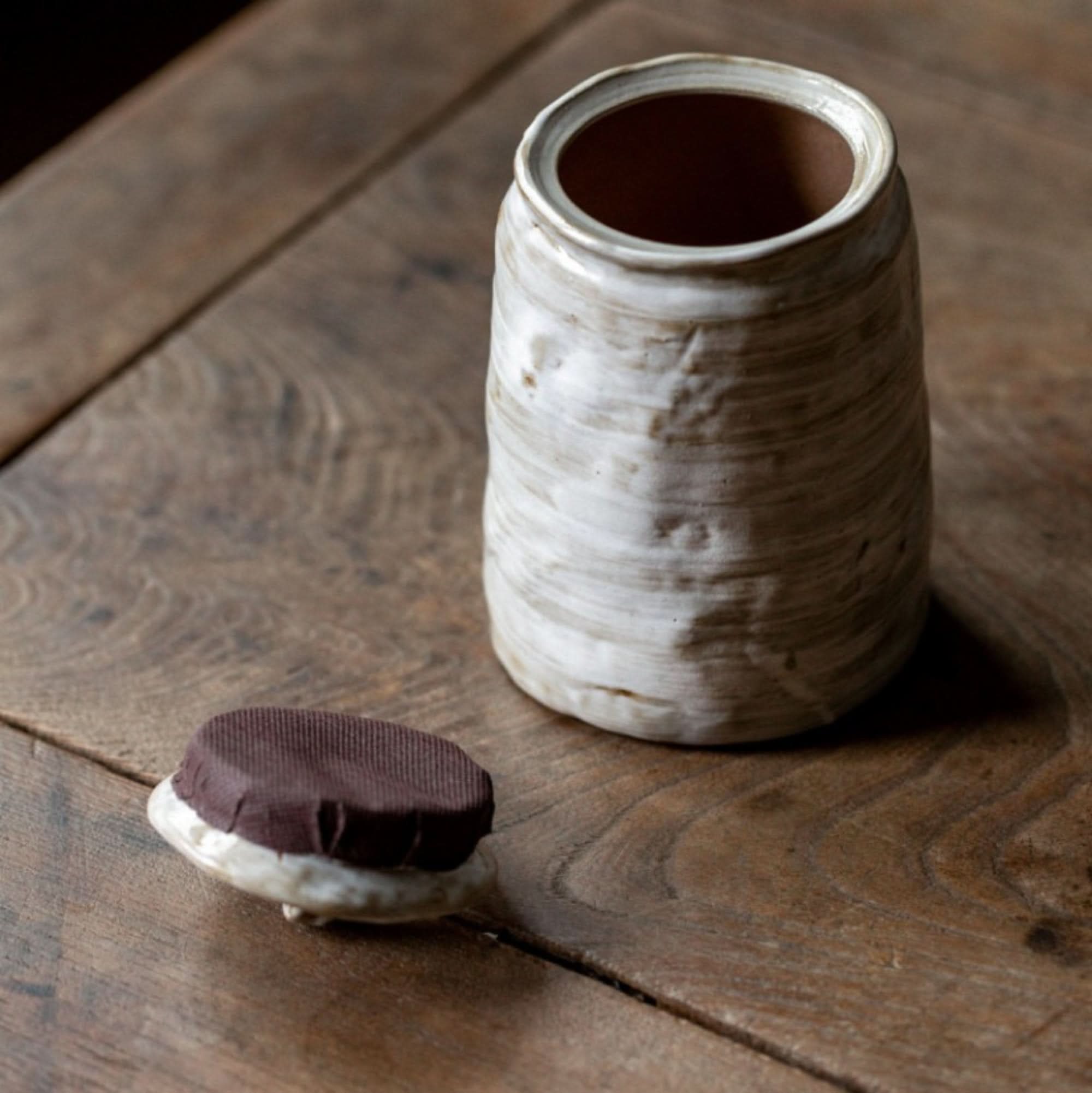 Rustic white stoneware tea canister with a brown lid on a wooden table.