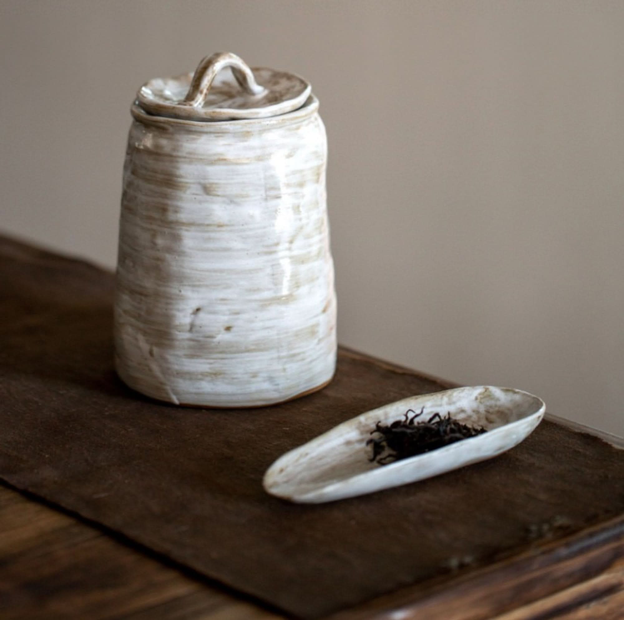 Textured white Stoneware Tea Canister with a small dish of tea leaves on a dark wood surface.