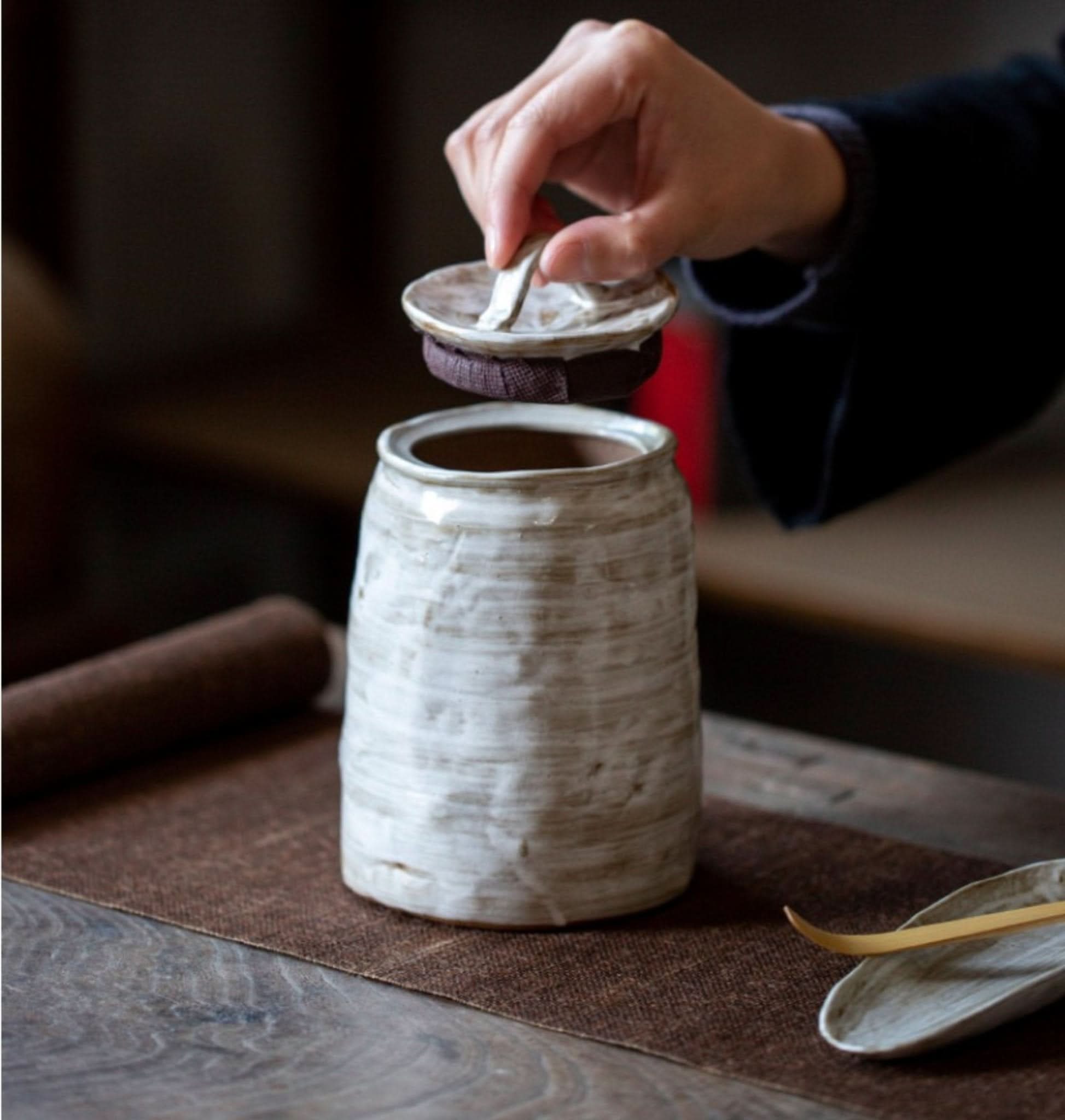 Hand placing lid on textured white stoneware tea canister. For tea, coffee, sugar, spices.