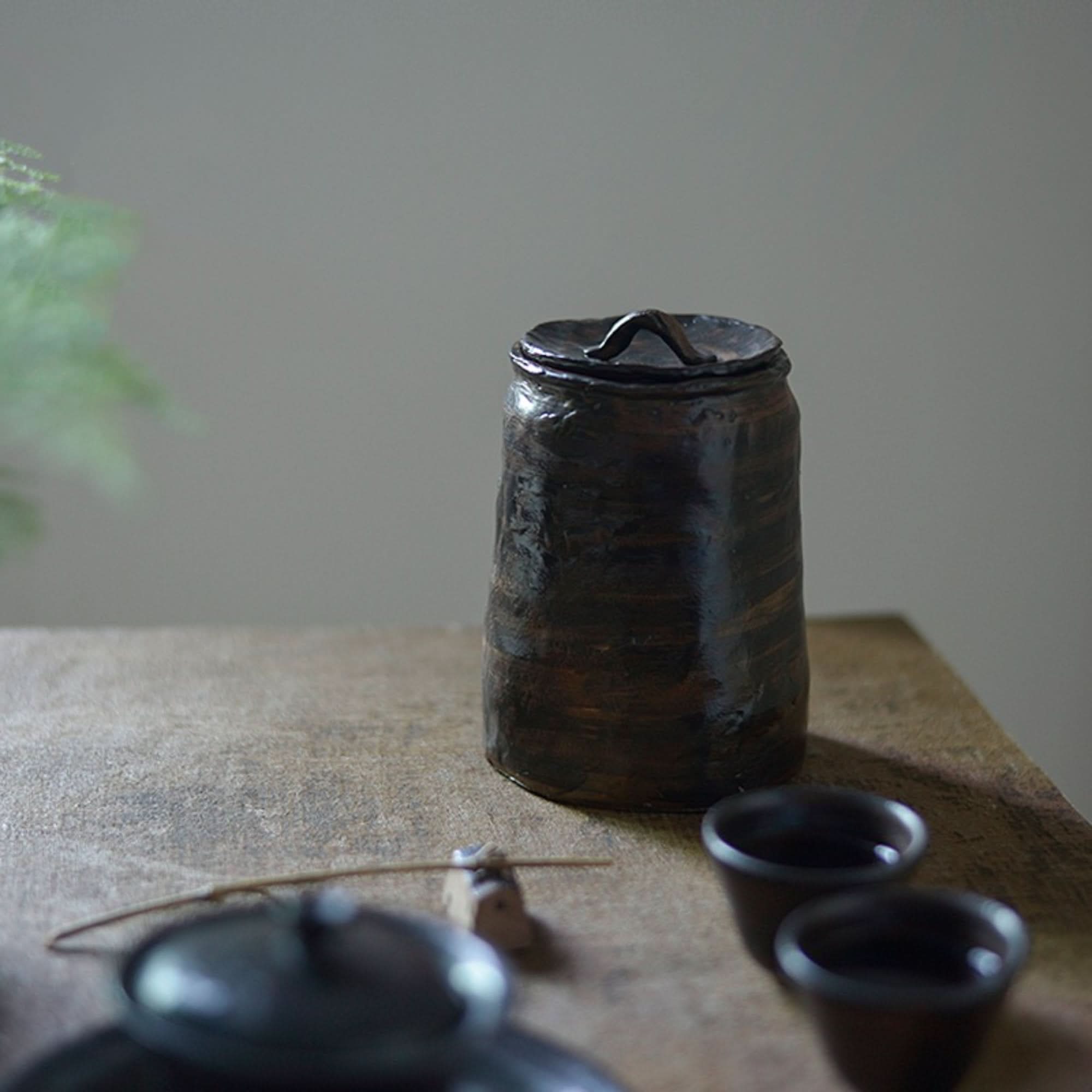 Dark brown stoneware tea canister with lid on rustic table, Gongfu tea set.