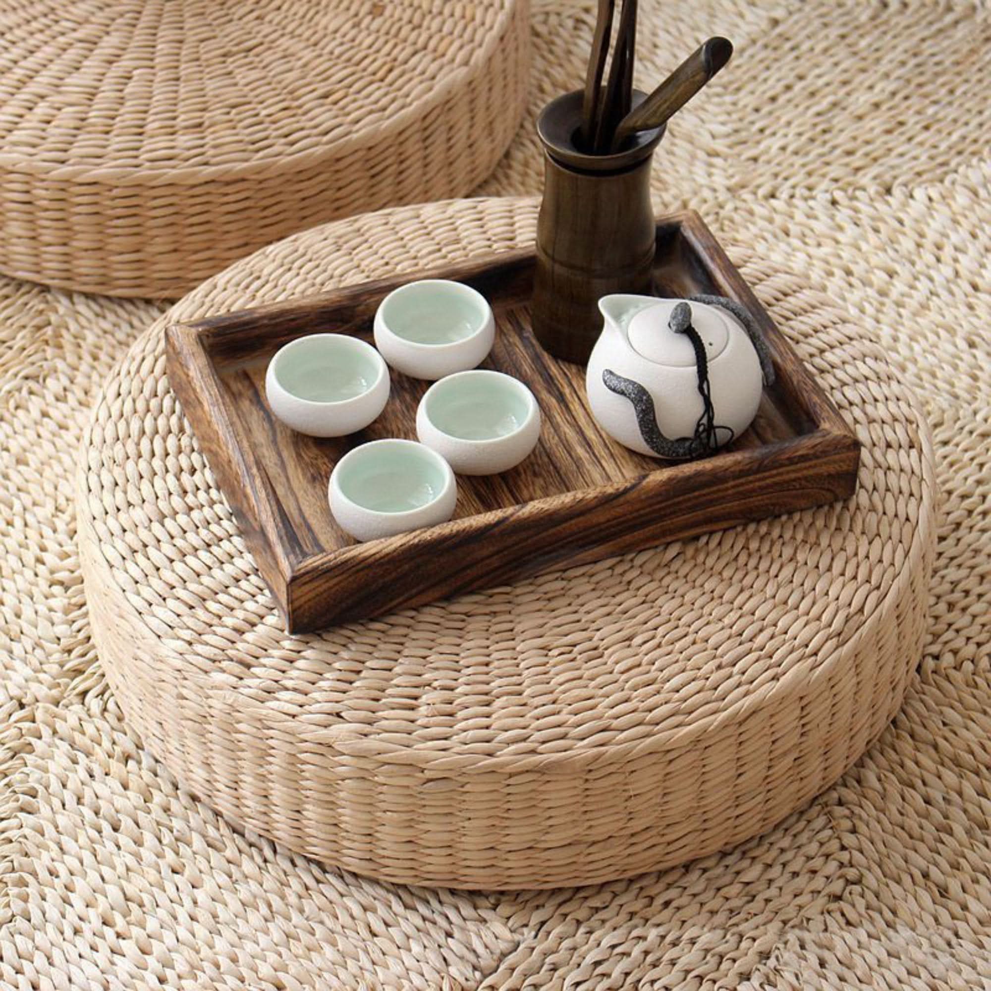 Straw floor pouf meditation cushion, with tea set on wooden tray, natural fiber decor.