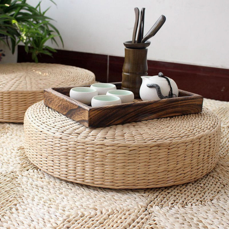 Natural straw floor pouf and meditation cushion with tea set on wooden tray.