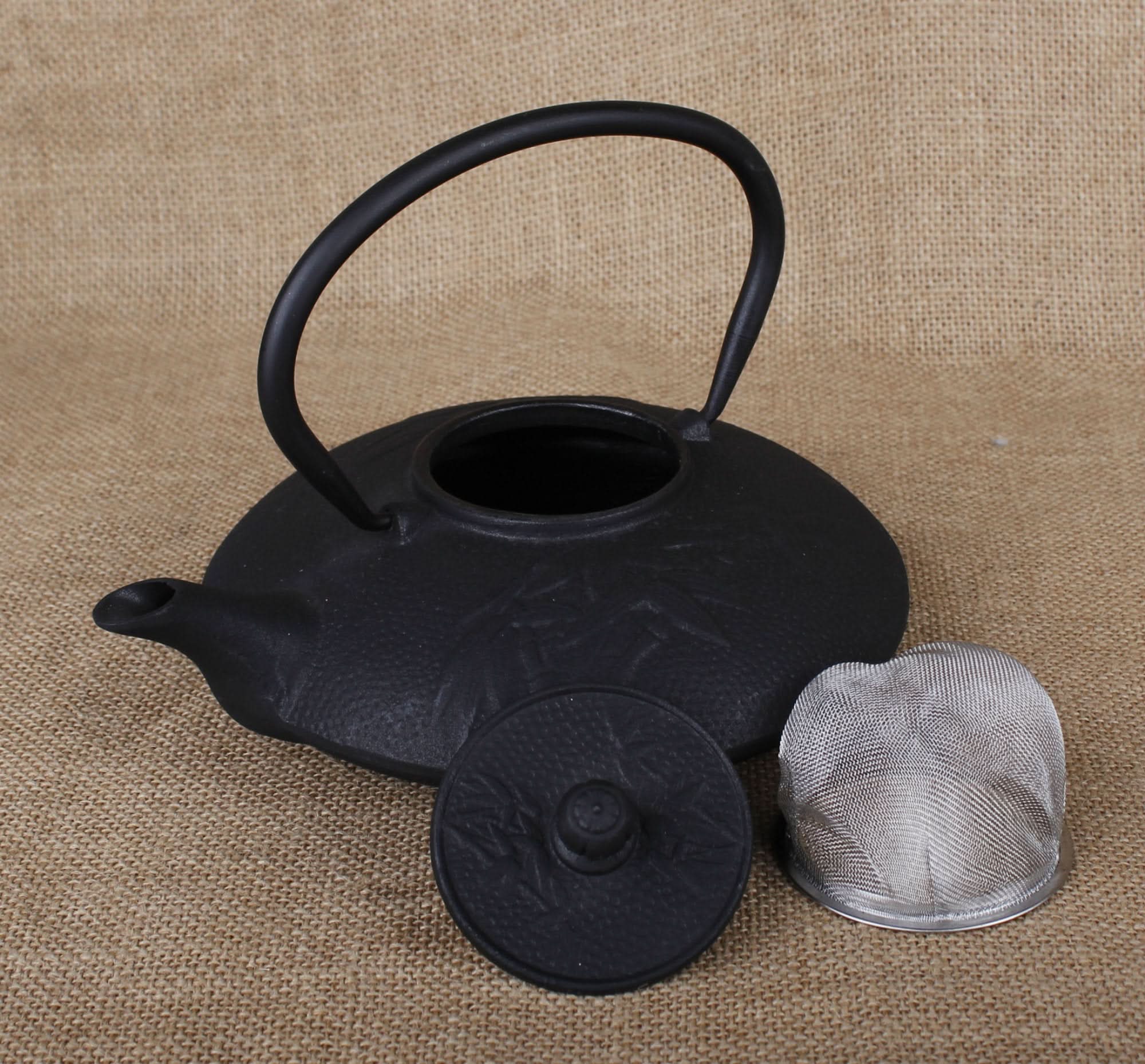Black cast iron tea kettle with strainer and lid on burlap background.