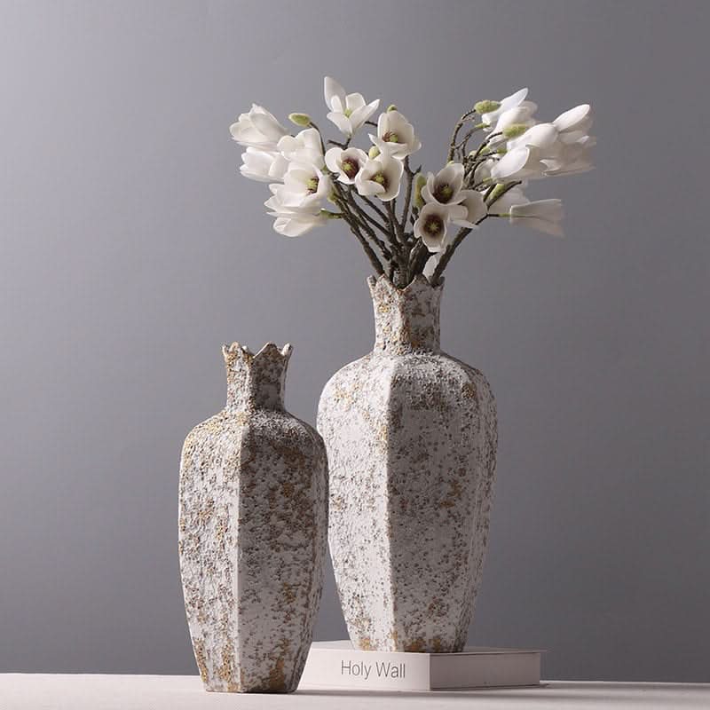 Textured stone vase with hexagonal shape, rustic white and gold finish, holding white flowers.