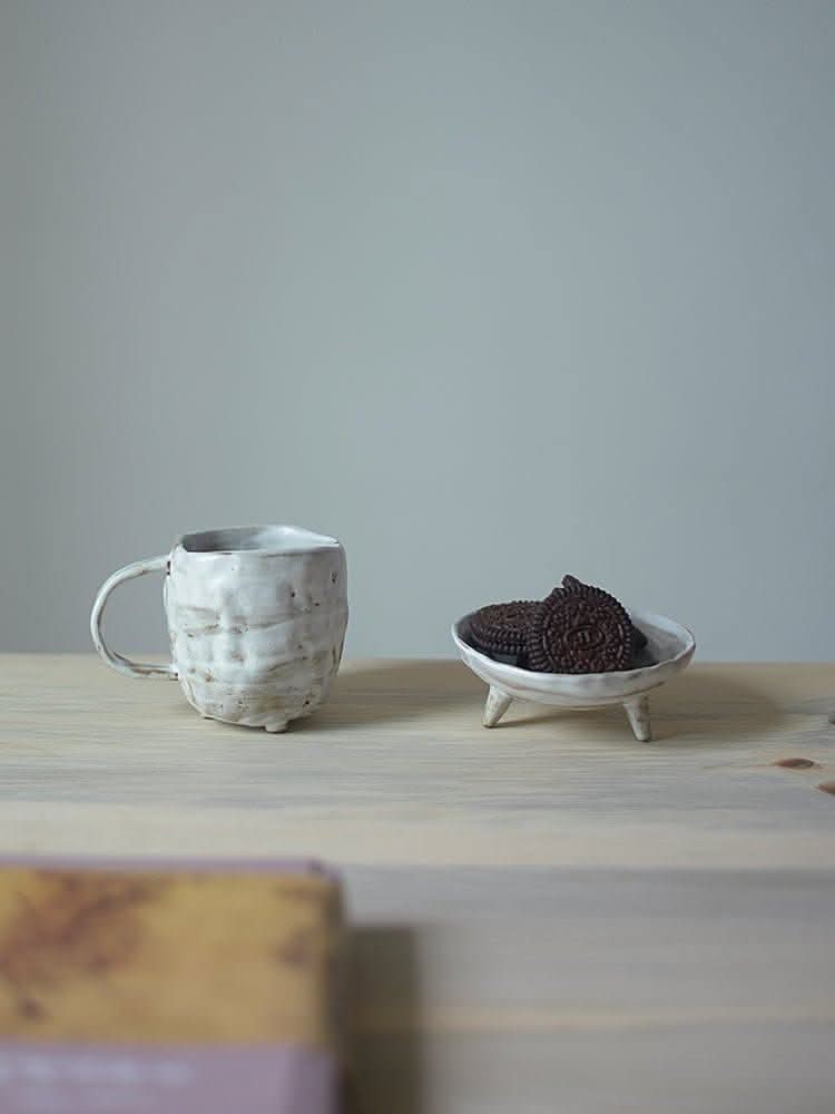 Tripod Stoneware Ceramic Irregular Fruit Bowl on wooden table with mug and cookies.