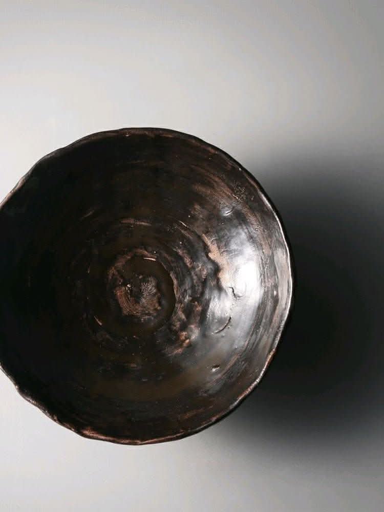 Dark brown Tripod Stoneware Ceramic Irregular Fruit Bowl on a light grey background.