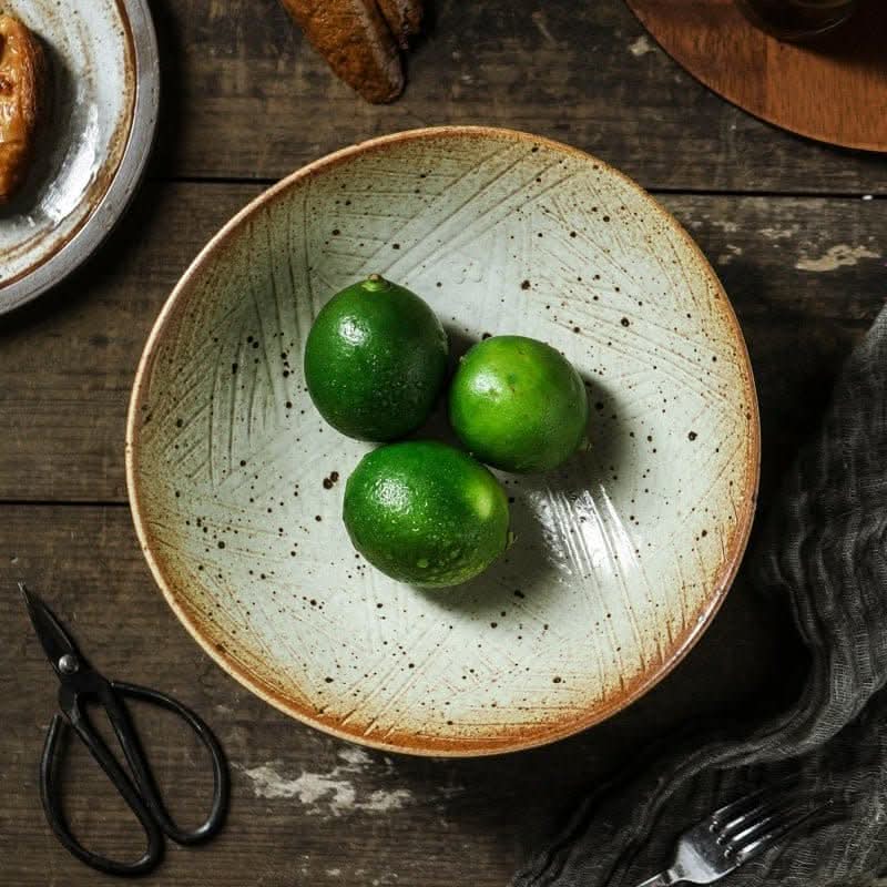 Rustic Tripod Stoneware Fruit Plate with three green limes on wooden table.