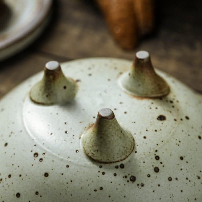 Light green speckled stoneware tripod fruit plate on rustic wooden surface.